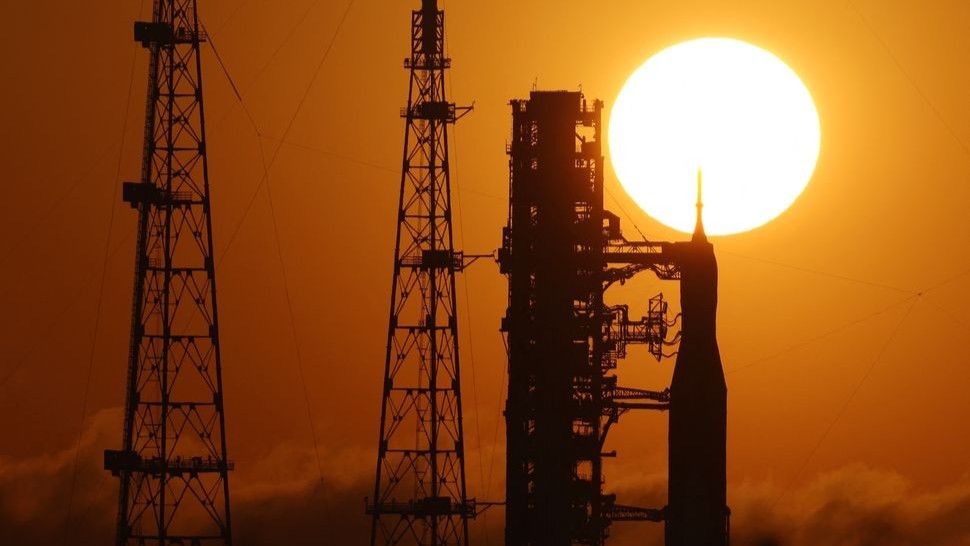 A rocket is stands in silhouette in front of a sunset.
