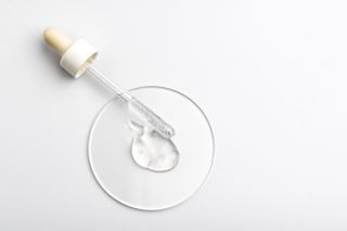 A glass pipette with viscous clear liquid spilling onto a glass circle