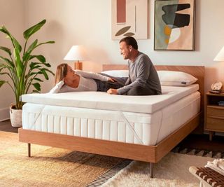 A man and a woman lying on the Tempur-Pedic Tempur-Adapt Topper on a mattress on a bed.