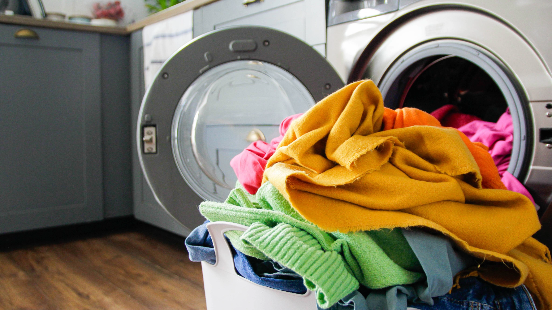 Pile of colorful clothes in a basket in front of a tumble dryer