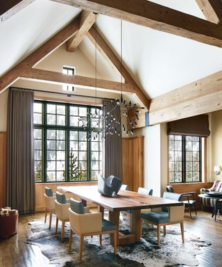 Dining room with vaulted ceiling, statement chandeliers, wooden table, leather chairs and hide rugs