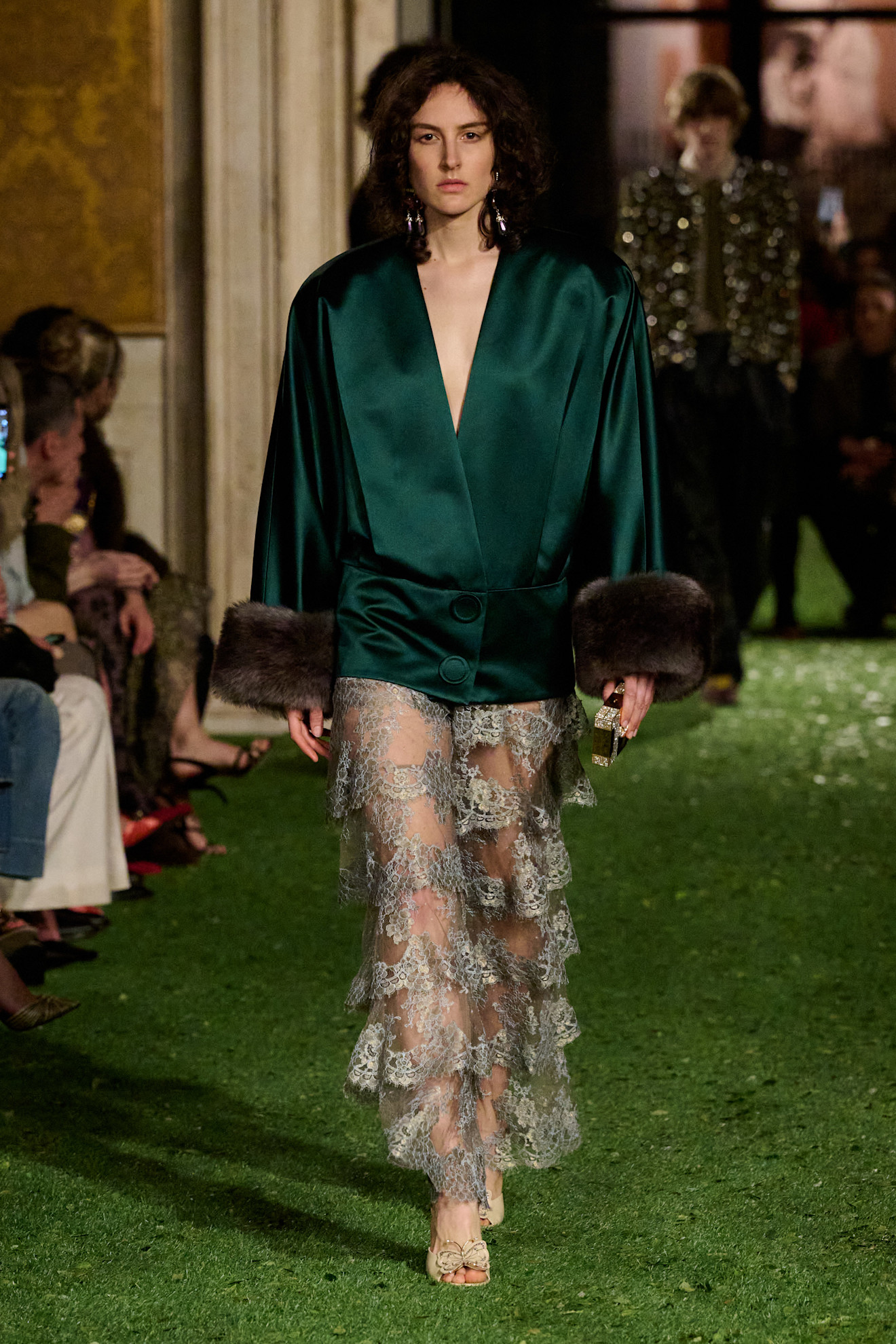 A model walking in the F/W 26 Valentino show wearing a green silk jacket with fur trim.