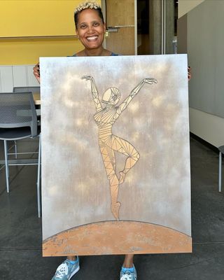 a woman holds a painting of a robot-like person dancing