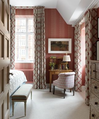 A bedroom with a cream carpet, a wooden dressing table and curtains with a lath and fascia heading and orange wallpapered walls