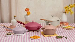 A selection of Our Place pots and pans laid out on a dining table with food, a tablecloth and flowers