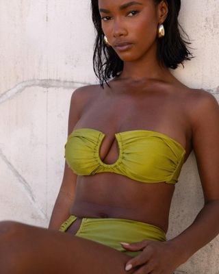 Model wearing olive green Villa Fresca cutout bikini, leaning against wall.