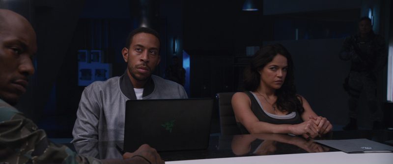 Ludacris and Michelle Rodriguez sitting at a table with a Razer laptop on it.