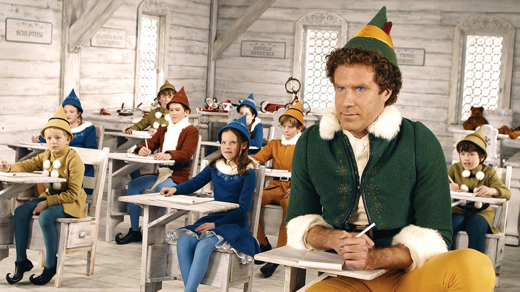 A still from the movie Elf, showing lots of children dresses as elves in a classroom and Will Ferrell dressed as an elf at the front.