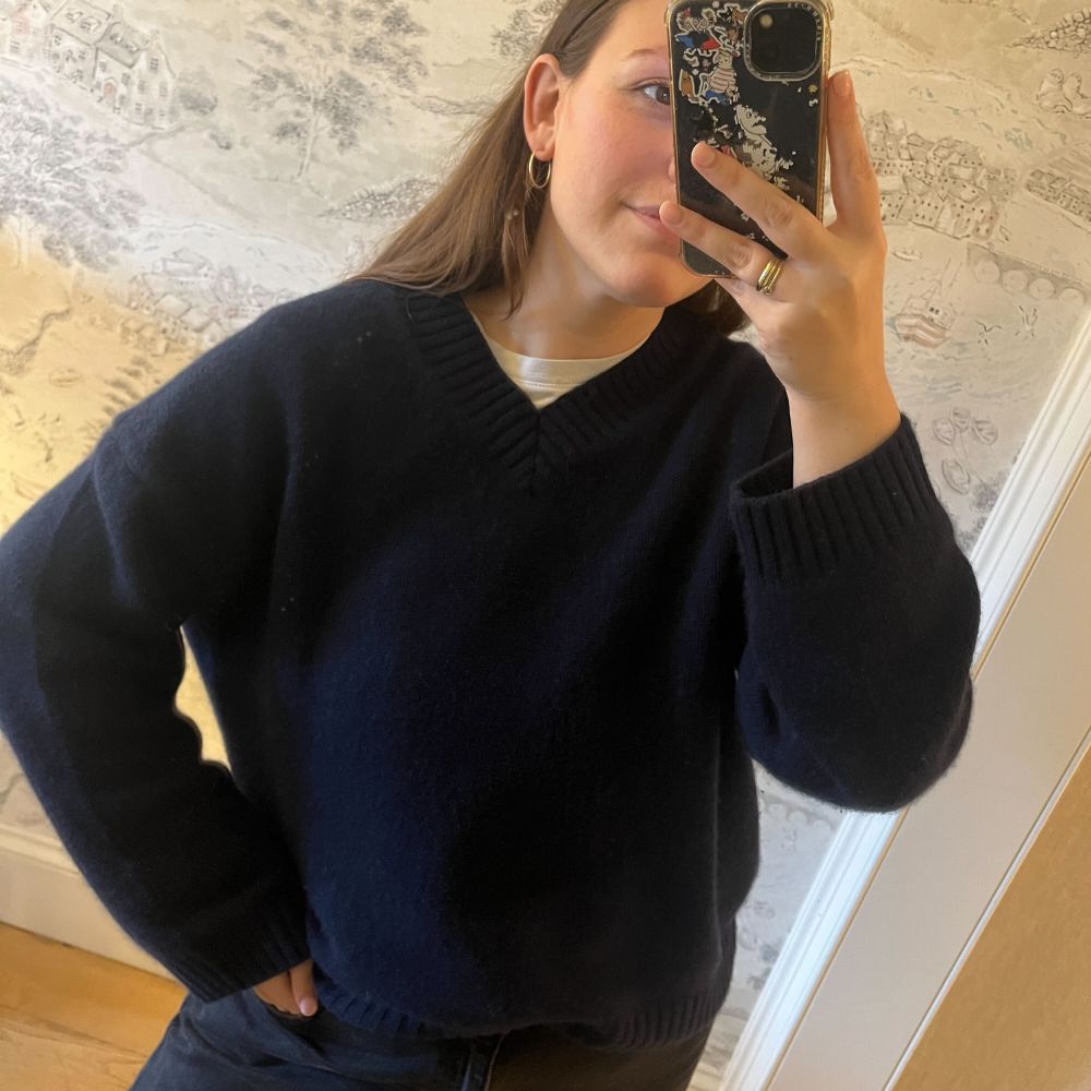 Who What Wear Managing Editor Poppy Nash wears a navy v-neck jumper and with black jeans.