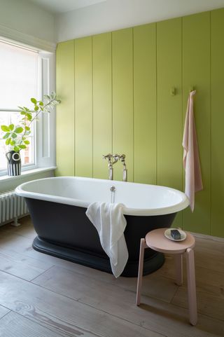 a bright green panelled wall behind a bath
