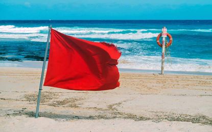 Red flag and lifebelt attached to pole on the beach. No swimming.