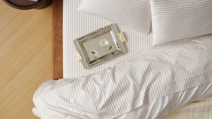 Brooklinen striped luxe sateen bedding and silver martini tray pictured from a bird's eye view inside of a neutral bedroom with hardwood floors