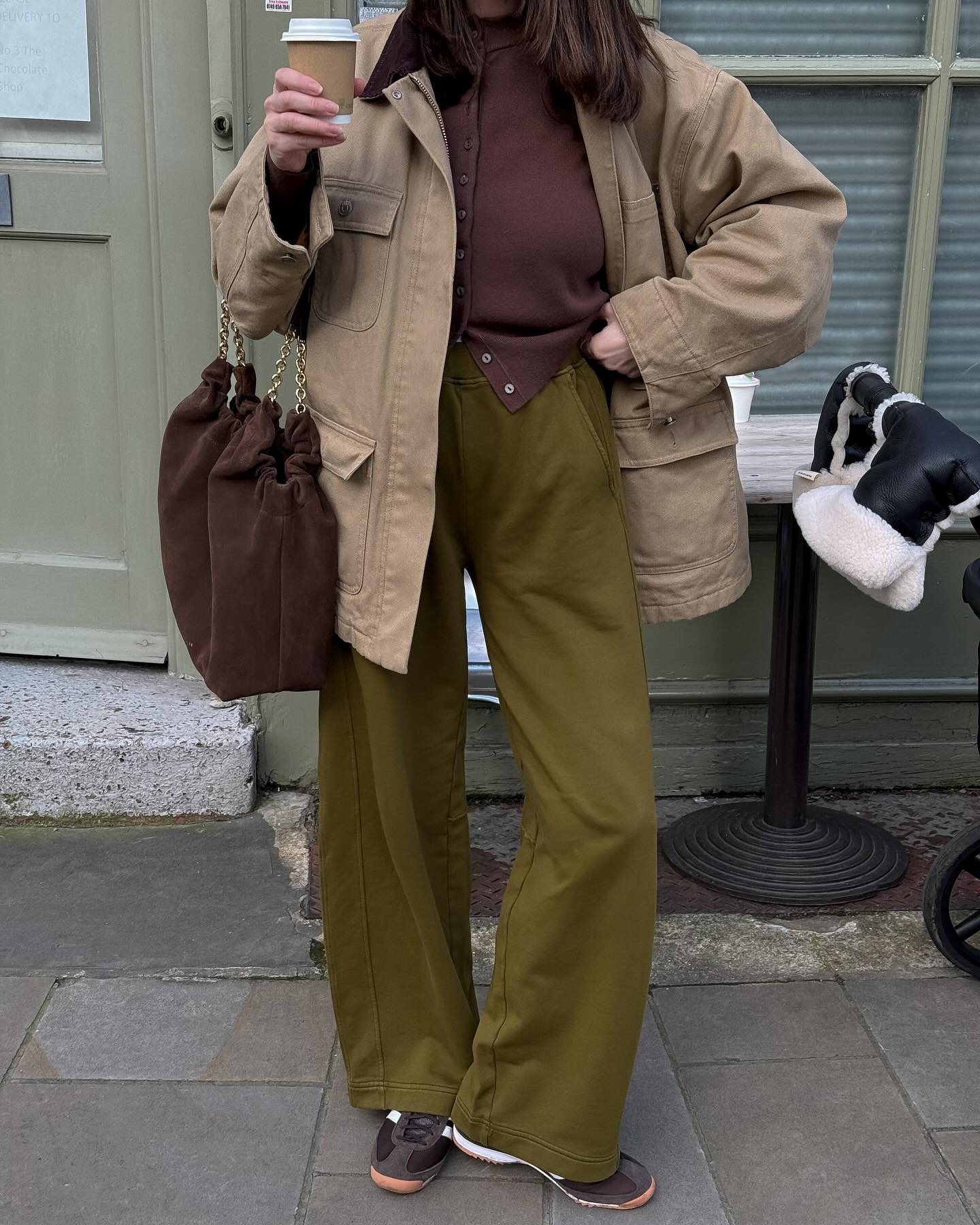 Woman wears beige coat, brown jumper, green trousers, brown trainers and brown suede bag