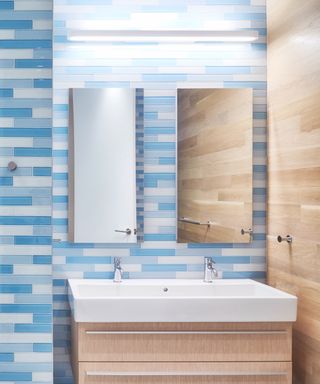 bathroom with blue and white tile shades, wall mounted vanity unit, twin mirrors, lighting,