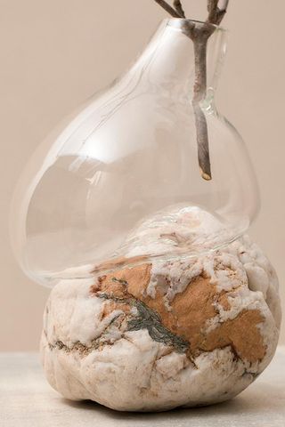 A clear glass vase that's blown around the rock in sand tones. There are tree branches in the vase.