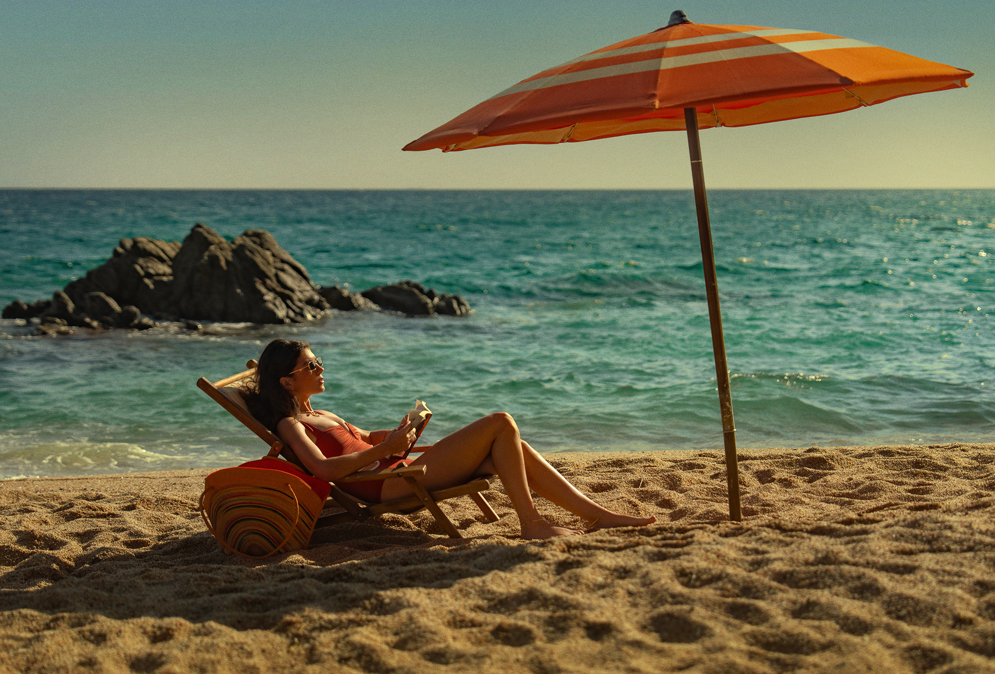 Film still from People We Meet on Vacation featuring character Poppy played by Emily Bader. She is reading a book on the beach under an umbrella.