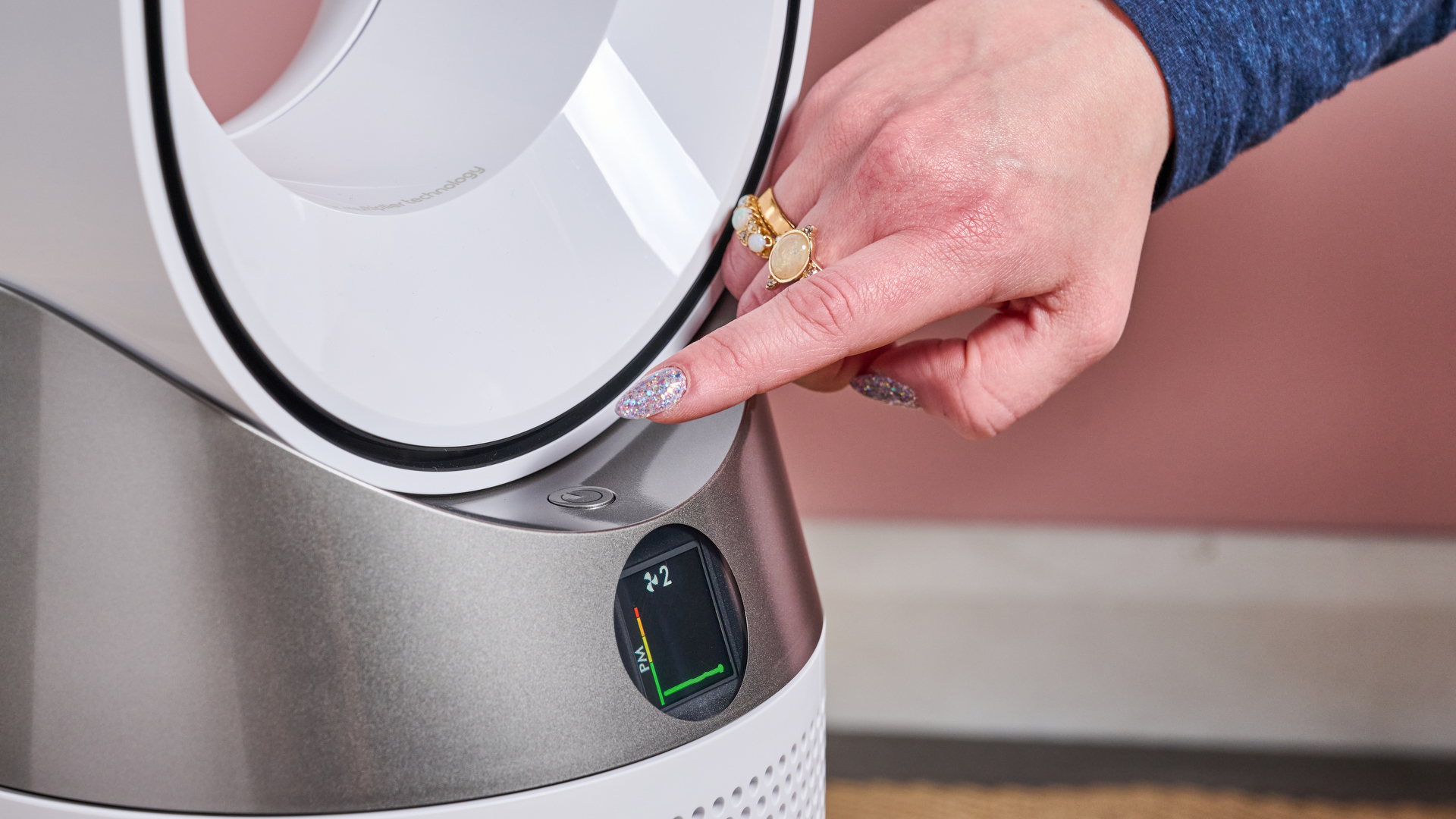 A woman is about to press the power button on the TP10 air purifier. The LCD screen shows the particle and that the fan is on speed two.