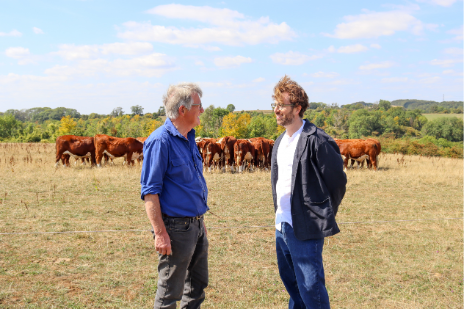Two men standing in a field with cows behind them discussing inheritance tax