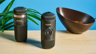 The Wacaco Nanopresso on a wooden surface with the Wacaco Barista Kit and some beans in the background