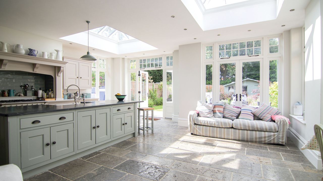 orangery with two skylights and glazed walls feautring a white kitchen and sofa