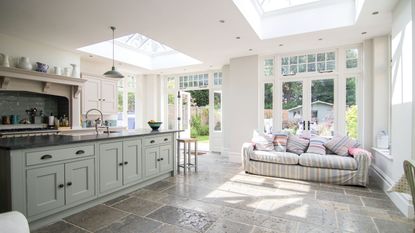 exterior image of stone house with cream oragnery with roof light leading onto a patio area and grass lawn