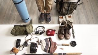 Low section of man standing with hiking and fishing gear arranged on table at home
