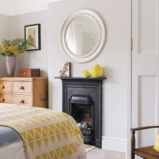 A grey bedroom with a wooden set of drawers and a small black fireplace. 