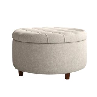 A circular beige storage ottoman with a tufted button top and dark brown legs underneath