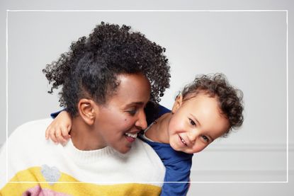 Mother smiling while young child hugs her from behind