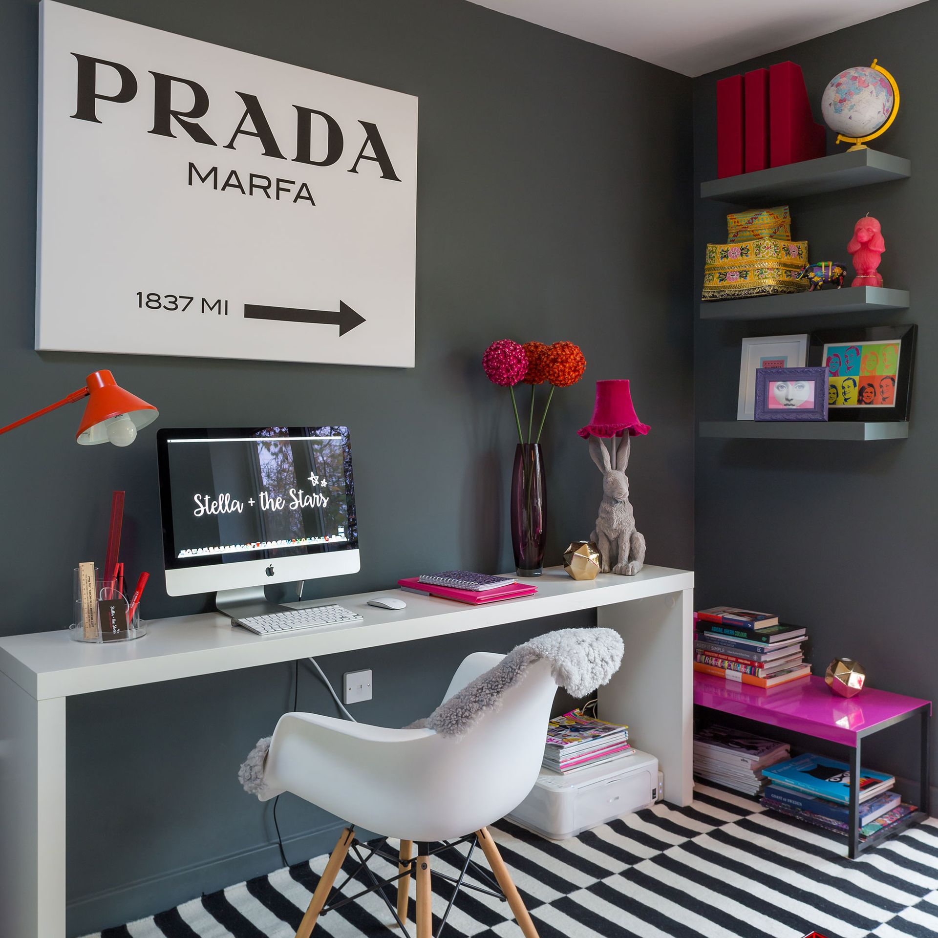 Grey home office with artwork, white desk, patterned rug and floating shelves painted to match the wall