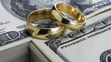 A pair of wedding rings sit on top of stacks of cash.