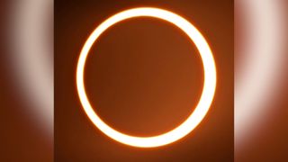 annular solar eclipse appears as a ring of fire in the sky. An orange glowing circle.