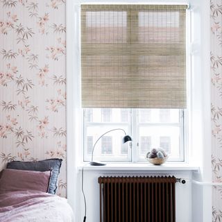 bamboo roller blinds in bedroom with black radiator and subtle pink floral patterned walls.jpg