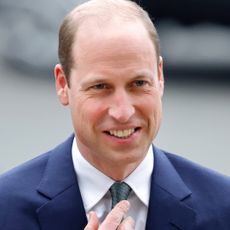 Prince William is clean shaven and wears a navy suit with a white shirt and blue tie