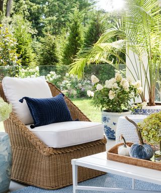 Patio with rattan armchair, white seating, blue cushions, coffee table, tray, flowers,