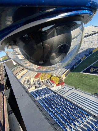 A JVC PTZ camera encased in a glass shell high above the West Virginia football field.