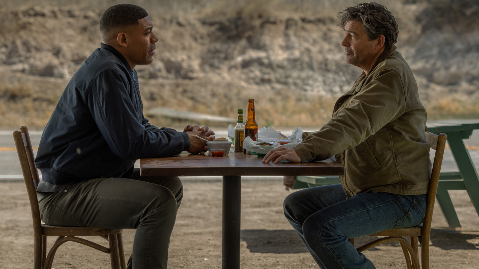 John Stewart and Hal Jordan sitting at a roadside table with food and drinks in Lanterns