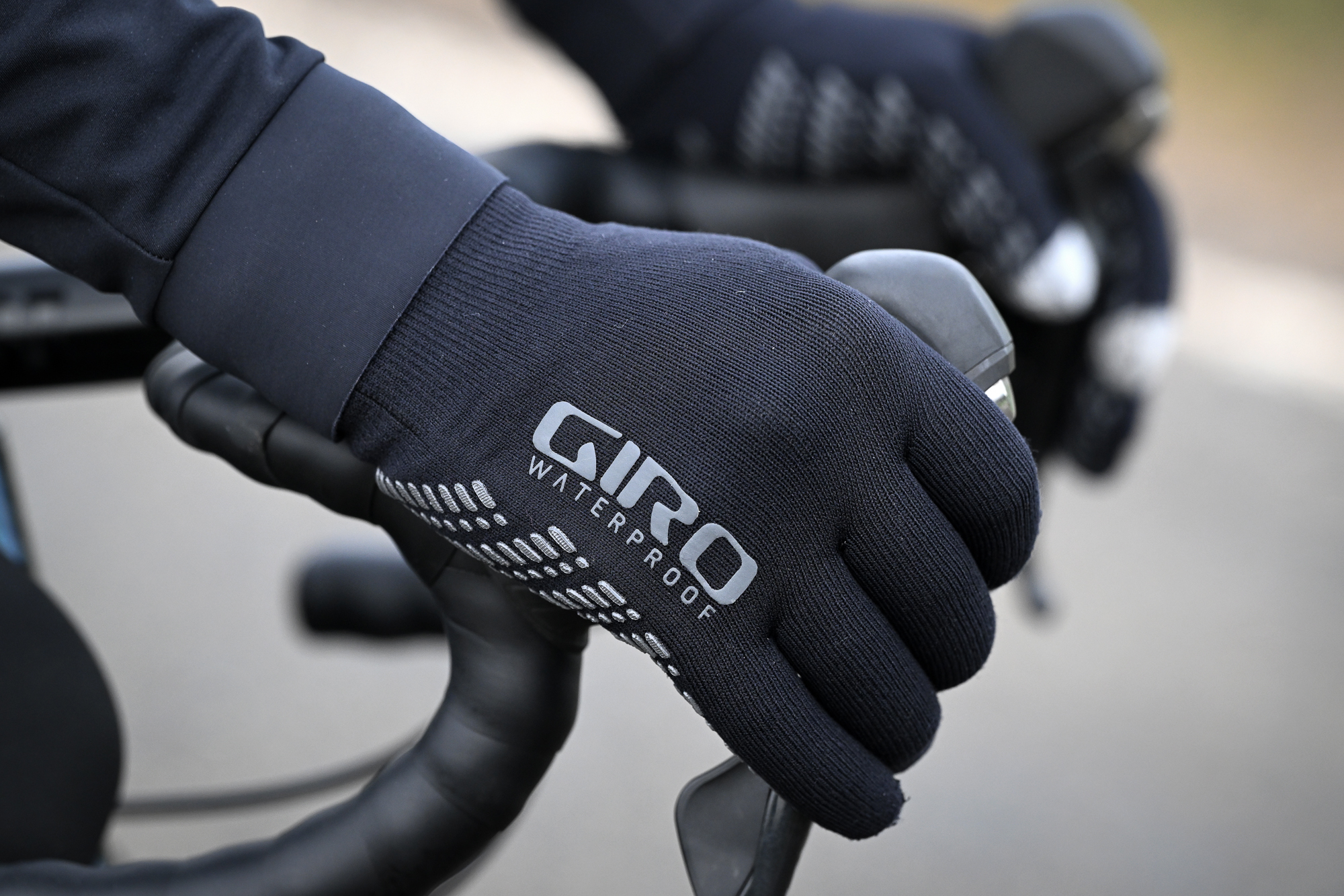 Closeup of hands wearing black gloves with the words 'Giro Waterproof' on them, holding some handlebars
