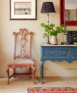 Cozy entryway with textured carpet, red patterned rug, blue console table, old fashioned chair, artwork and mirror on wall