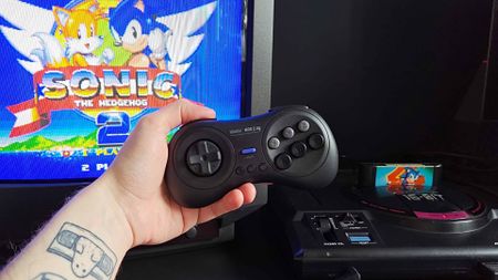 Hand holding 8Bitdo M30 Sega Mega Drive/Genesis controller with Sonic the Hedgehog 2 title on Sony Trinitron CRT TV next to Japanese console.