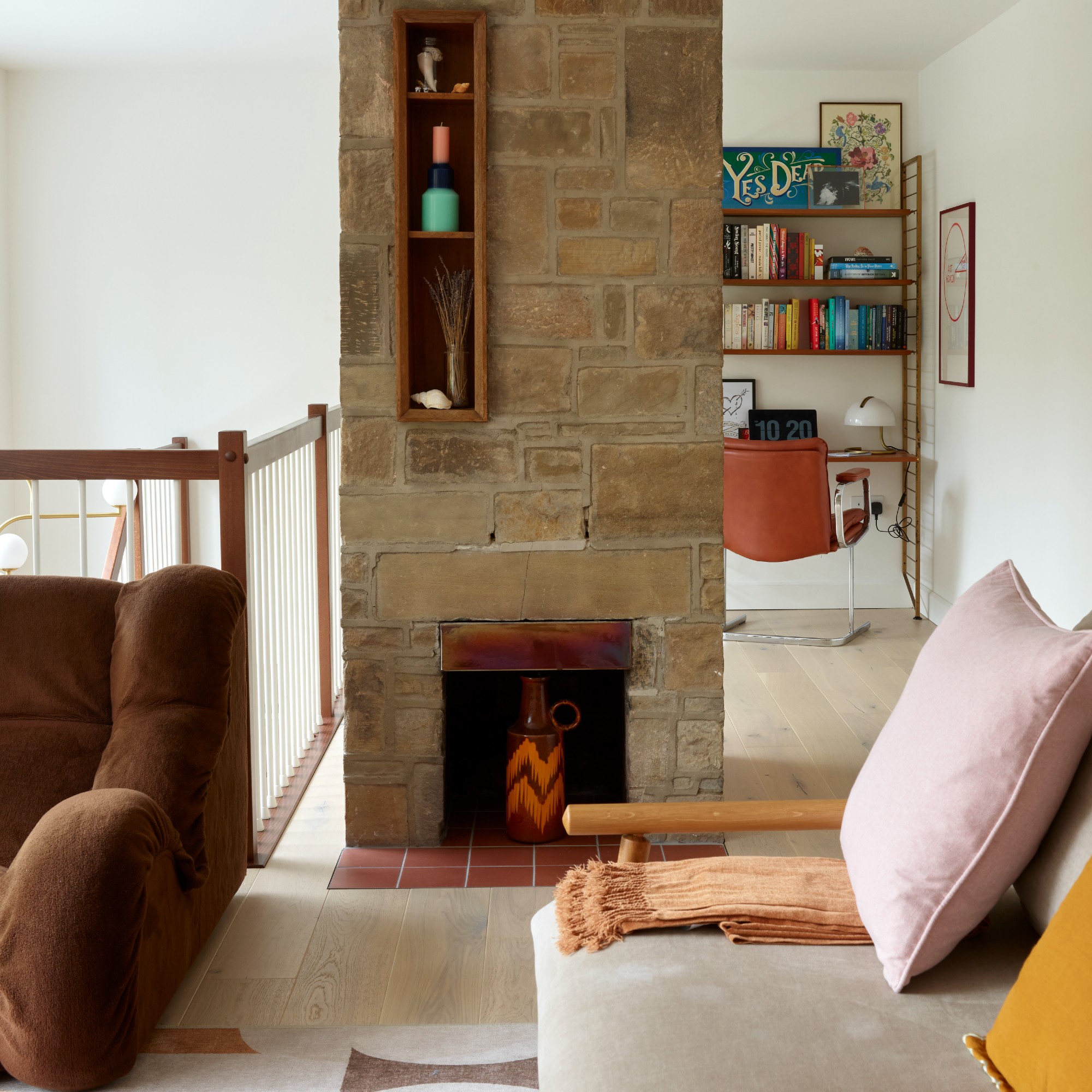 An airy living room with a low-profile brown sofa, a neutral sofa with a wooden frame and a shelf displaying a few decorative items