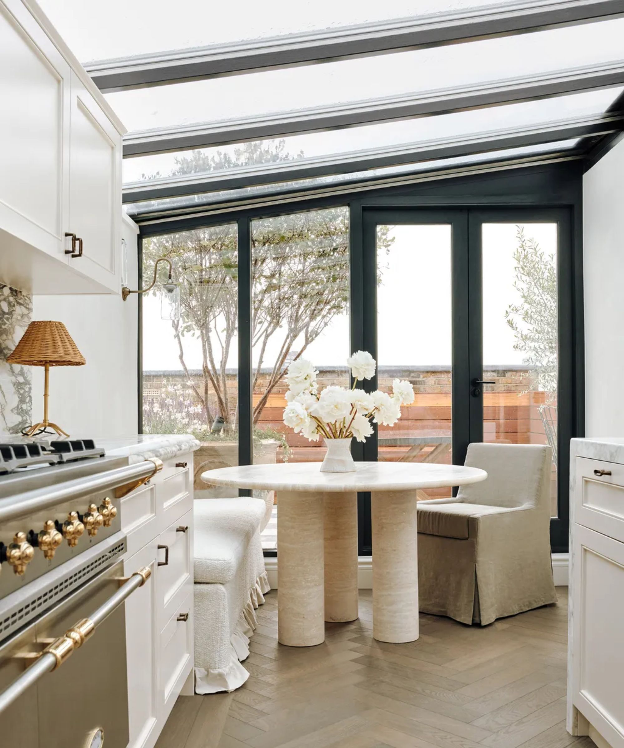Modern white and cream kitchen with round dining table and upholstered chairs. Wooden flooring, white marble countertops and cabinets with cooker in forground