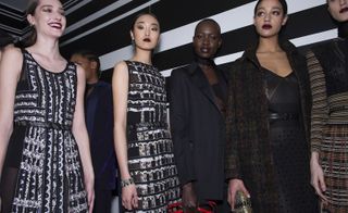 Six female models wearing looks from Bottega Veneta's collection. Two models are wearing black and white patterned, semi-sheer dresses. Another model is wearing a dark blue piece and neck scarf. The fourth model is wearing a black jacket, neck scarf and black piece with cut out design. The fifth model is wearing a black dress with spotted design, a belt and a dark brown patterned coat. And the sixth model is wearing a black and multicoloured striped and plaid style piece