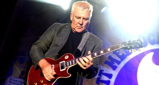 Alex Lifeson wears a gray blazer and takes a solo on his red Les Paul Axcess.