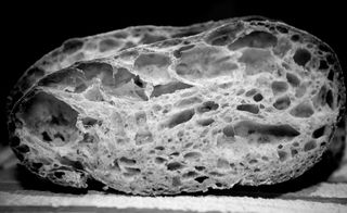 A black and white photo of an oval shaped and cut load of bread.