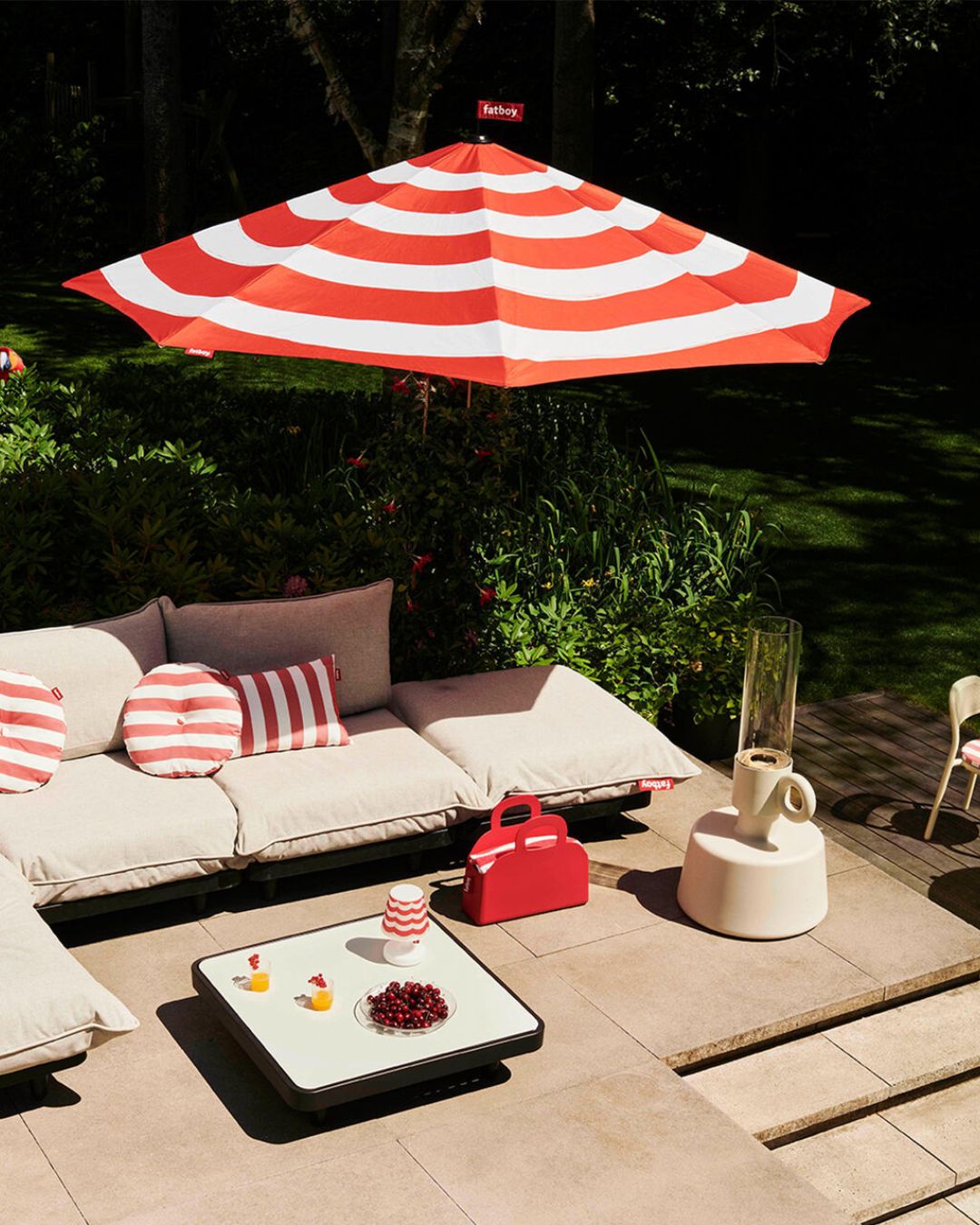 Stripesol Red in a sun-filled pool patio with an outdoor modular sofa in beige, striped cushions, a red bag and striped coffee table lamp.