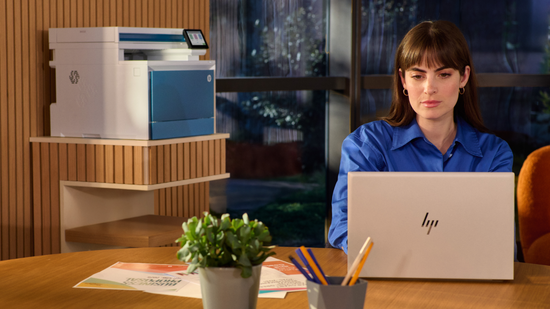 A woman using a HP laptop in a modern office, with a HP Color LaserJet Enterprise MFP 4801fw printer in the background
