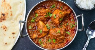 Spicy curry in metal bowl with naan bread