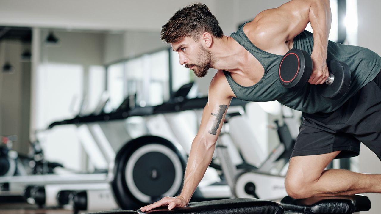 Man performing a dumbbell row over a gym bench