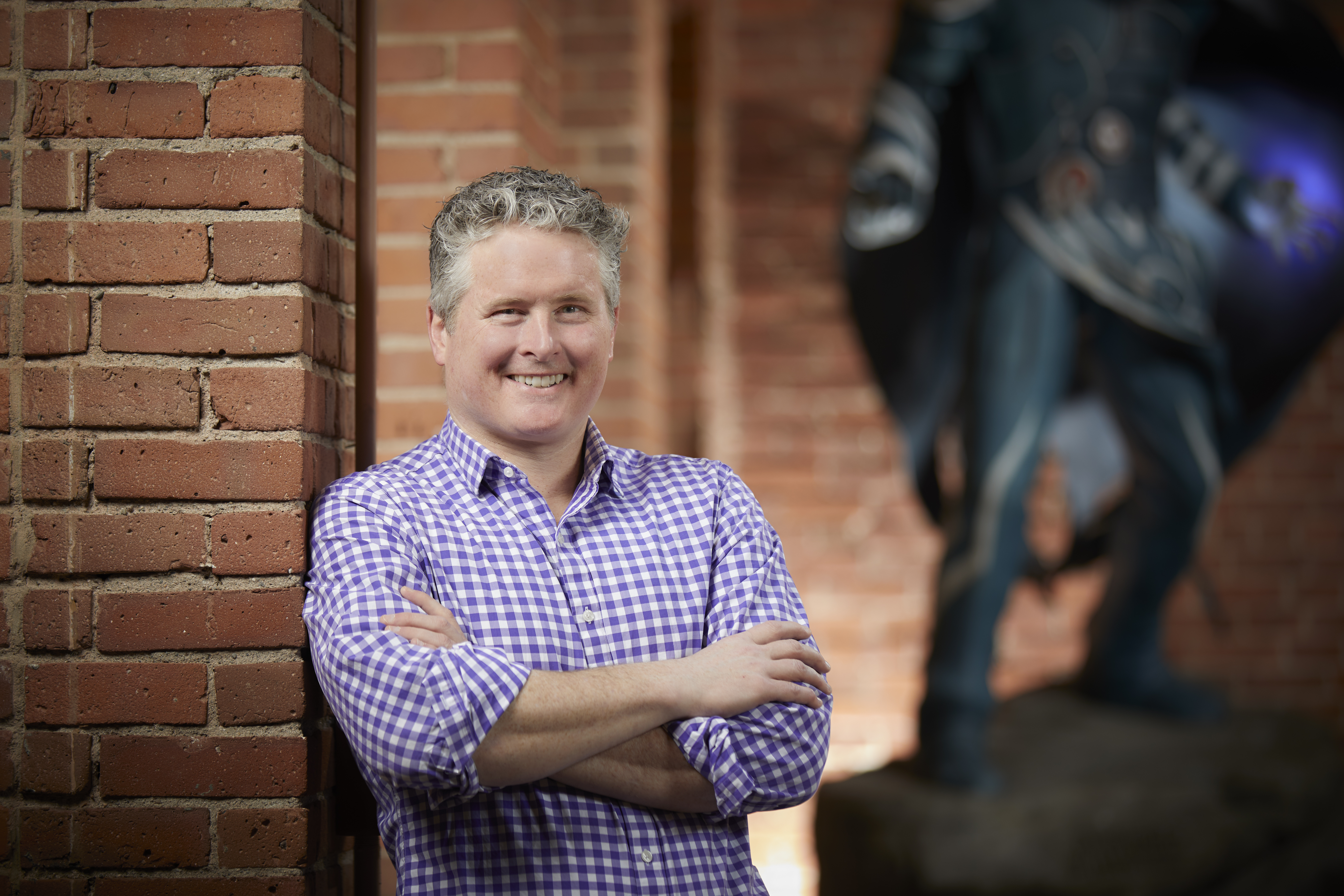 Chris Cocks smiling and leaning against a brick pillar, with a statue visible in the background
